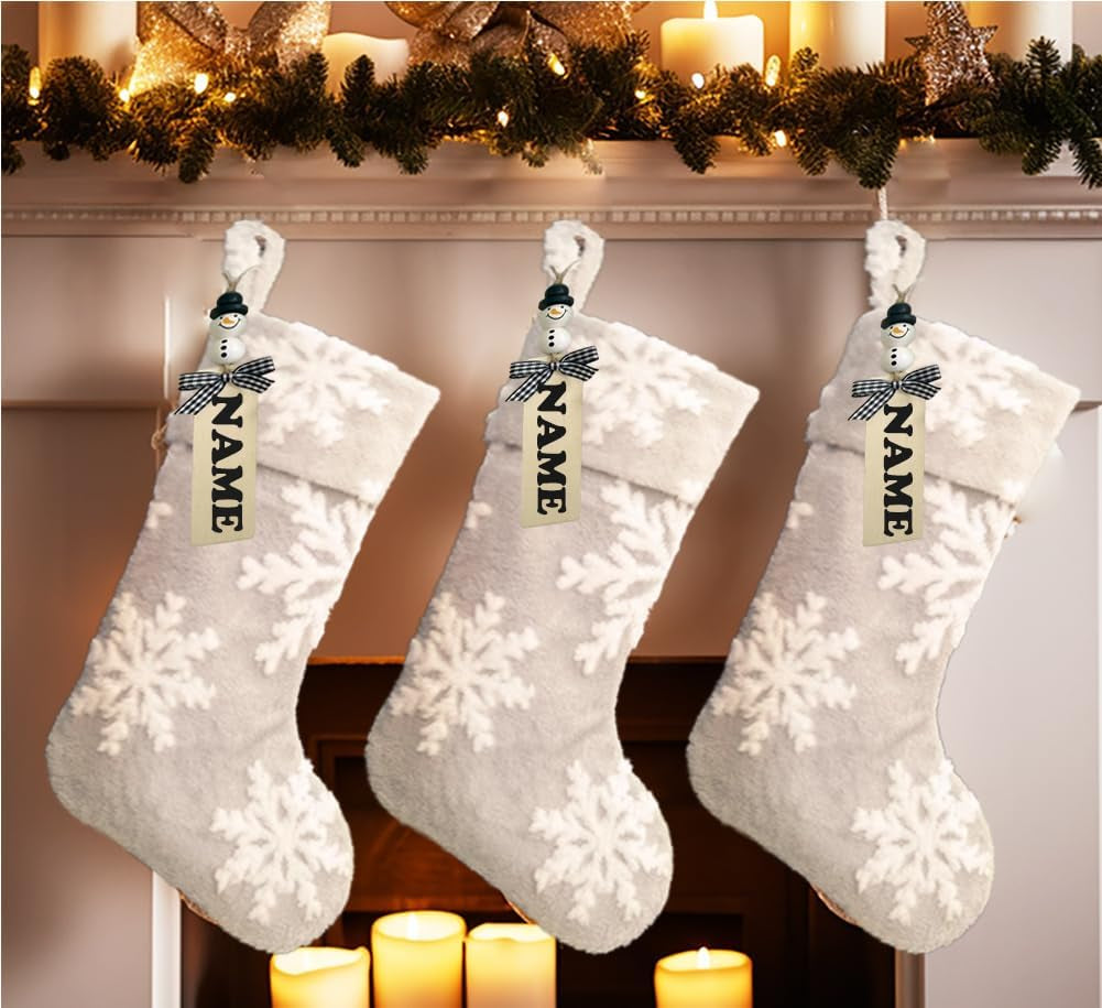 Three white Christmas stockings with snowflake patterns hanging on a fireplace mantle decorated with candles and greenery.