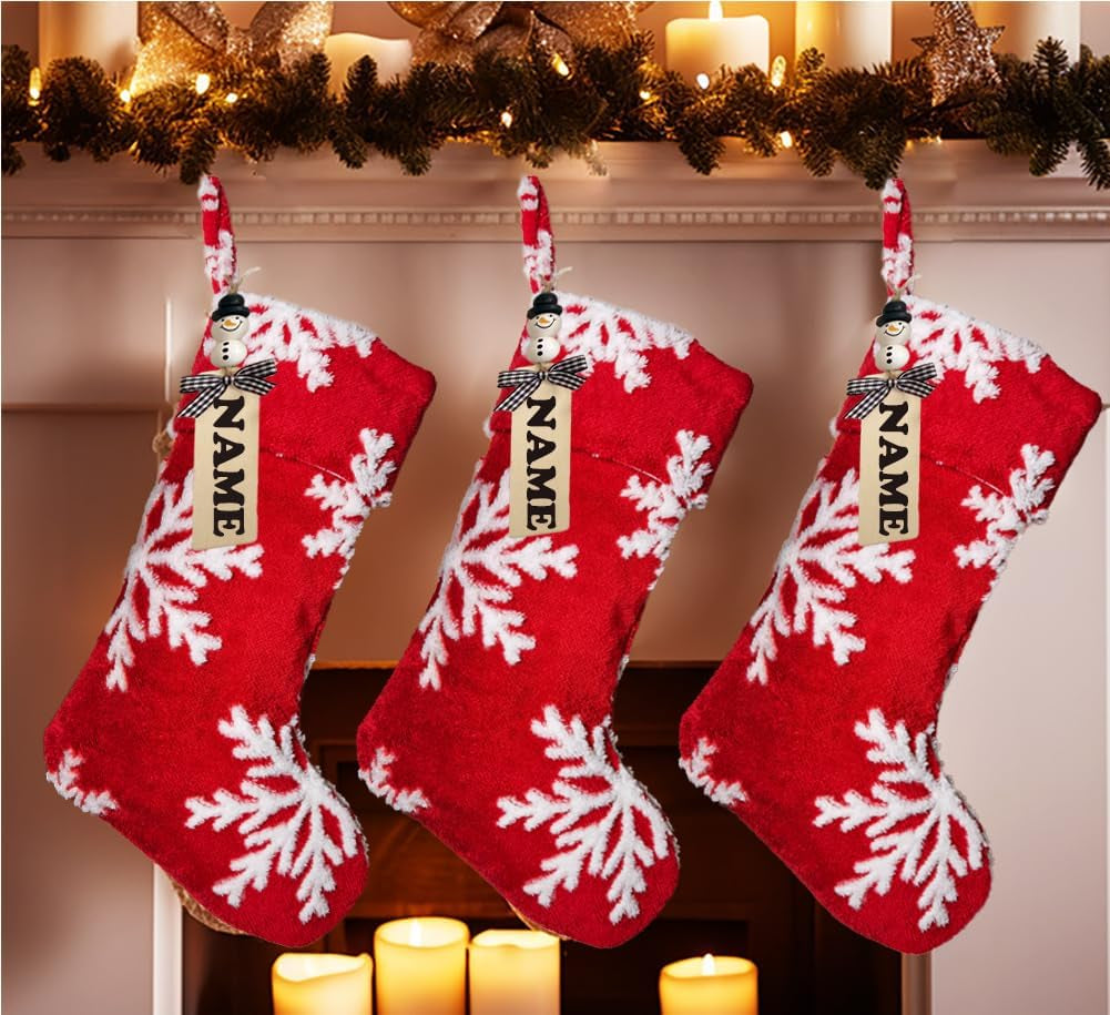 Three red Christmas stockings with white snowflake patterns hanging on a fireplace mantle.