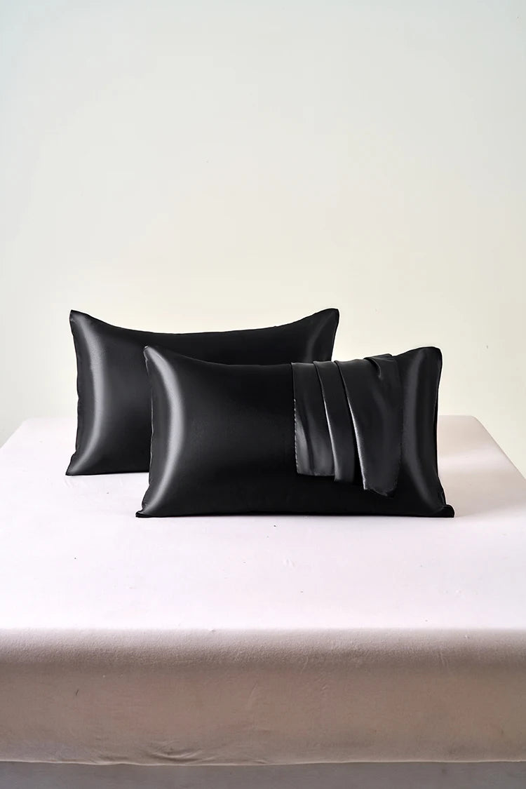 Two black satin pillows on a white surface with a white background