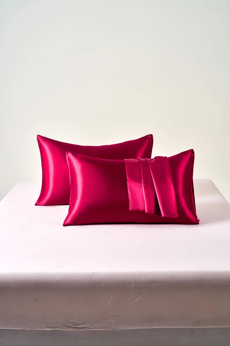 Two bright pink satin pillows on a white surface with a light gray background