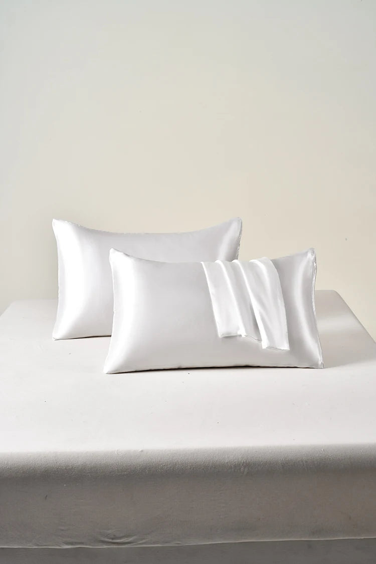 Set of white satin pillowcases on a bed with a plain background