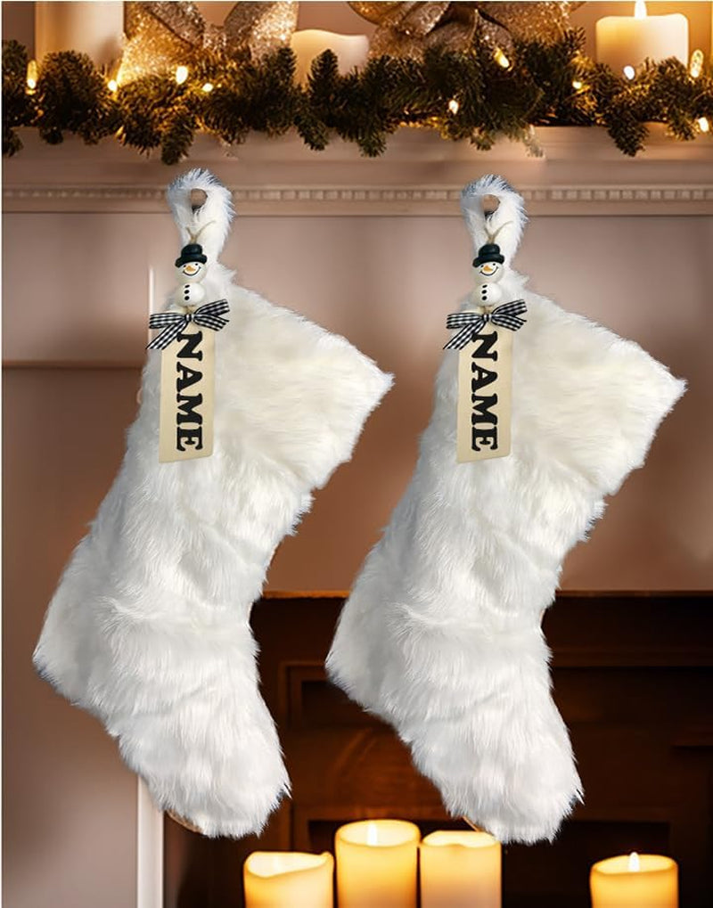 Two white feathered stockings with 'NAME' tags hanging on a fireplace mantel.