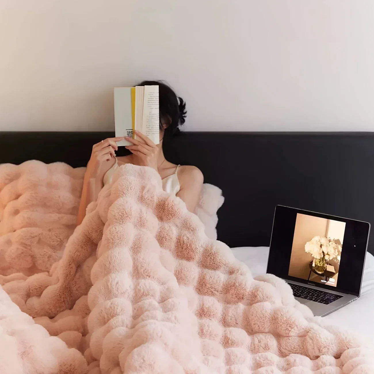 Cozy Pink Pom Pom Blanket draped over a person reading a book in bed.
