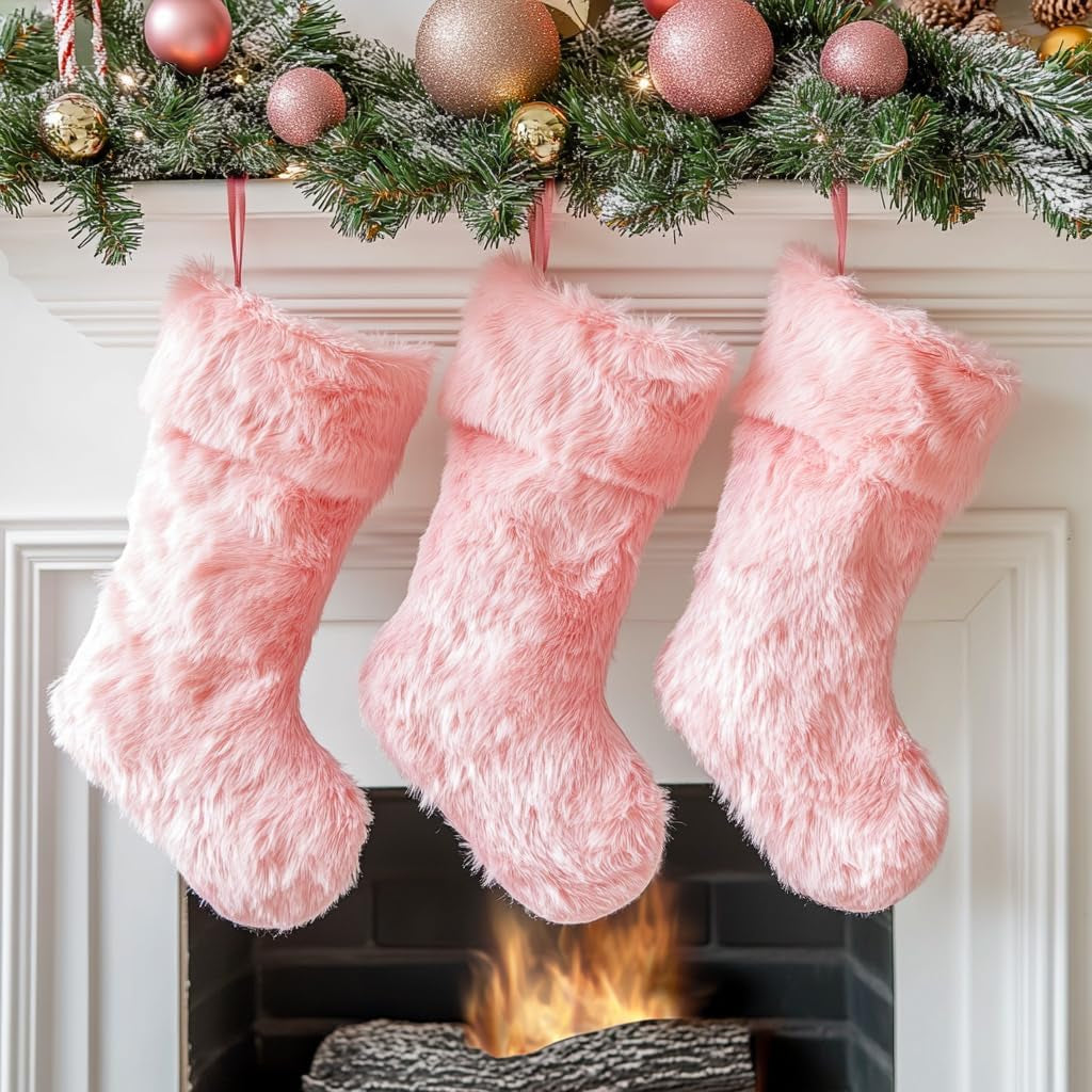 Three pink fuzzy stockings hanging above a fireplace with Christmas decorations.